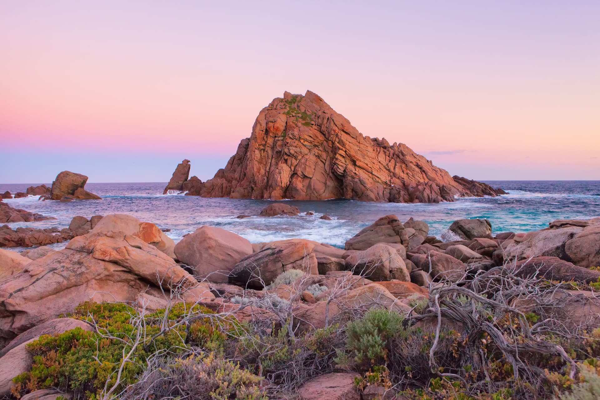 A coastal rock formation in the sea at sunset with pink clouds