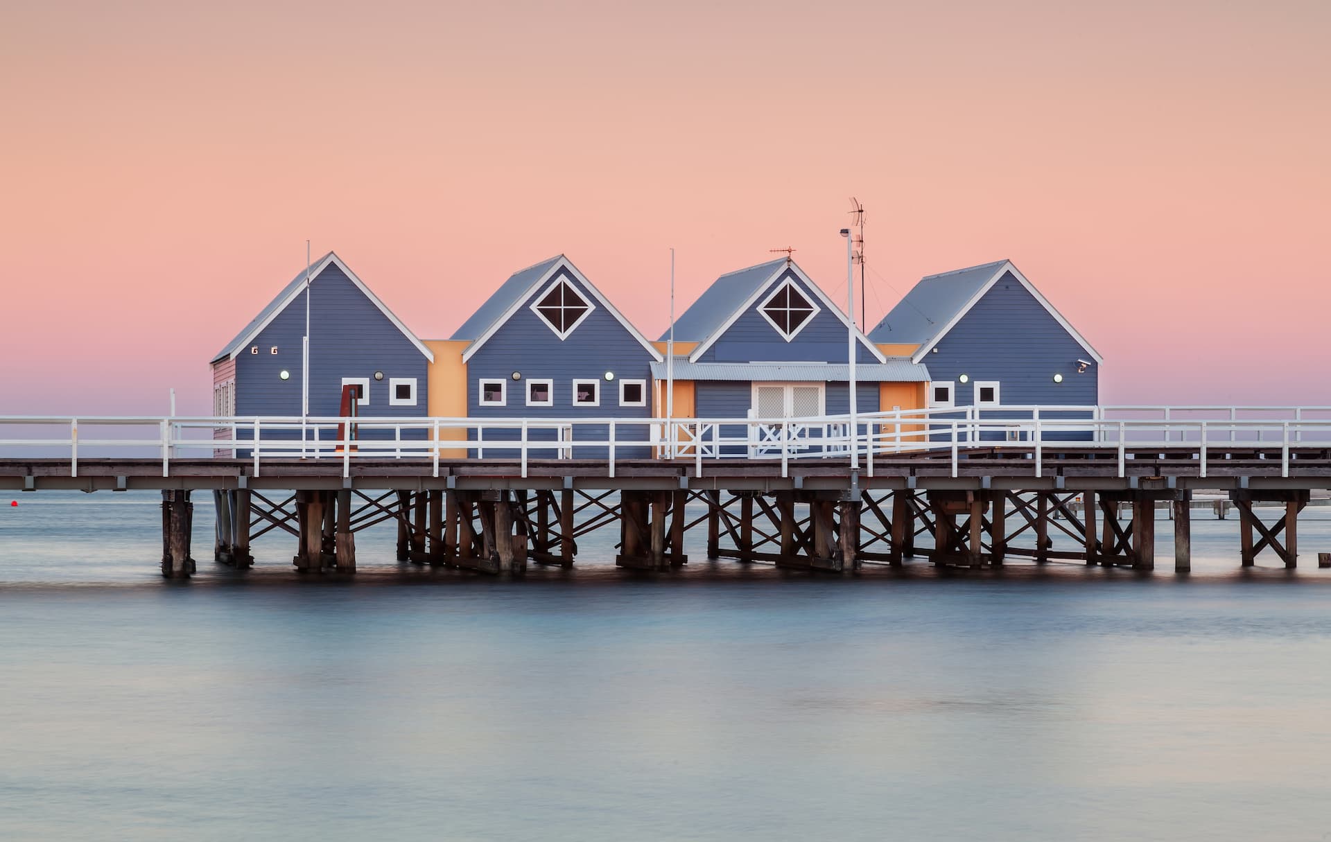 Blue wooden houses built on a pier over calm water at dusk